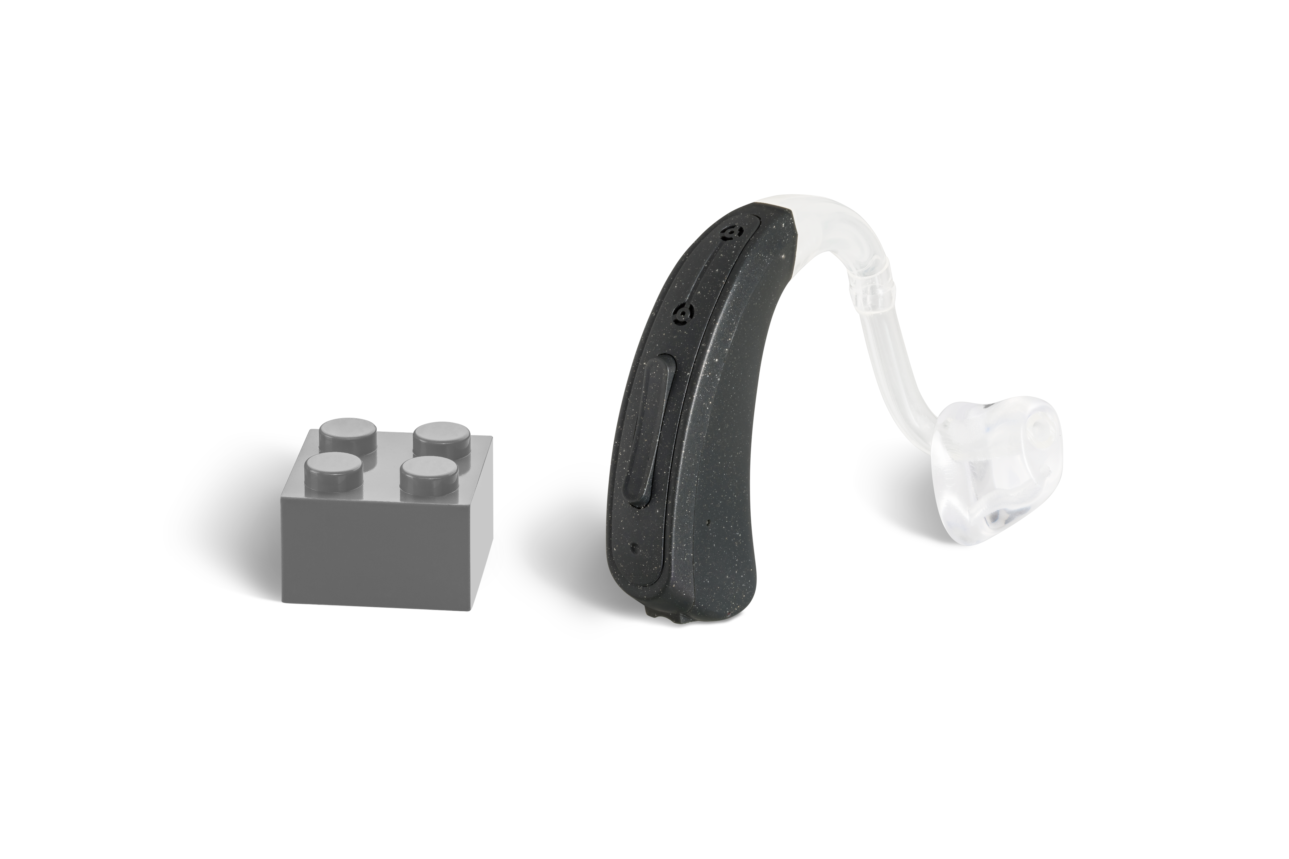 Das Hörgerät KINDaluna 1200 als Bauform Hinter dem Ohr mit Energieversorgung Batterie neben einem grauen Klemmbaustein stehend auf weißem Hintergrund.