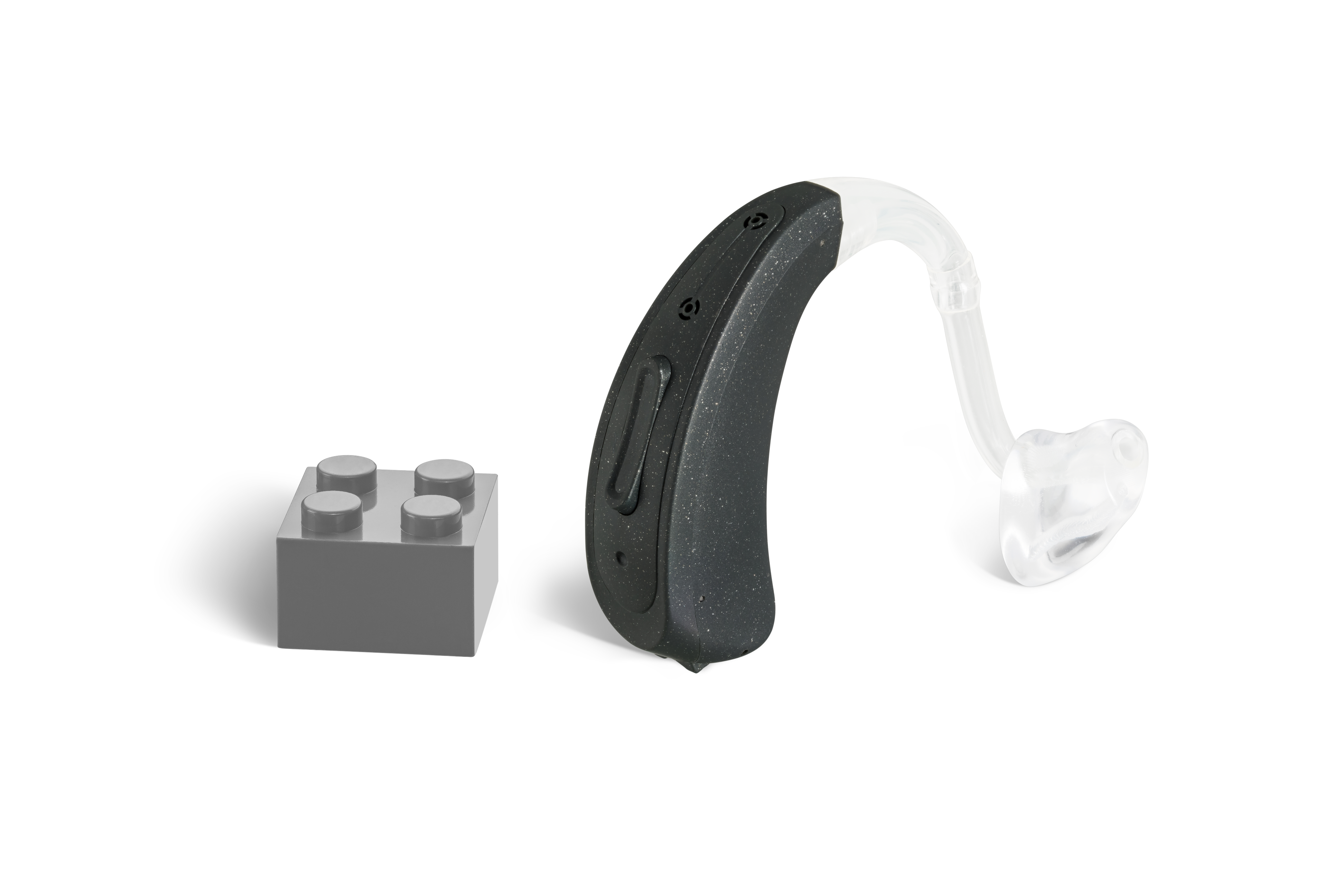 Das Hörgerät KINDaluna 1100 als Bauform Power HdO mit Energieversorgung Batterie neben einem grauen Klemmbaustein stehend auf weißem Hintergrund.