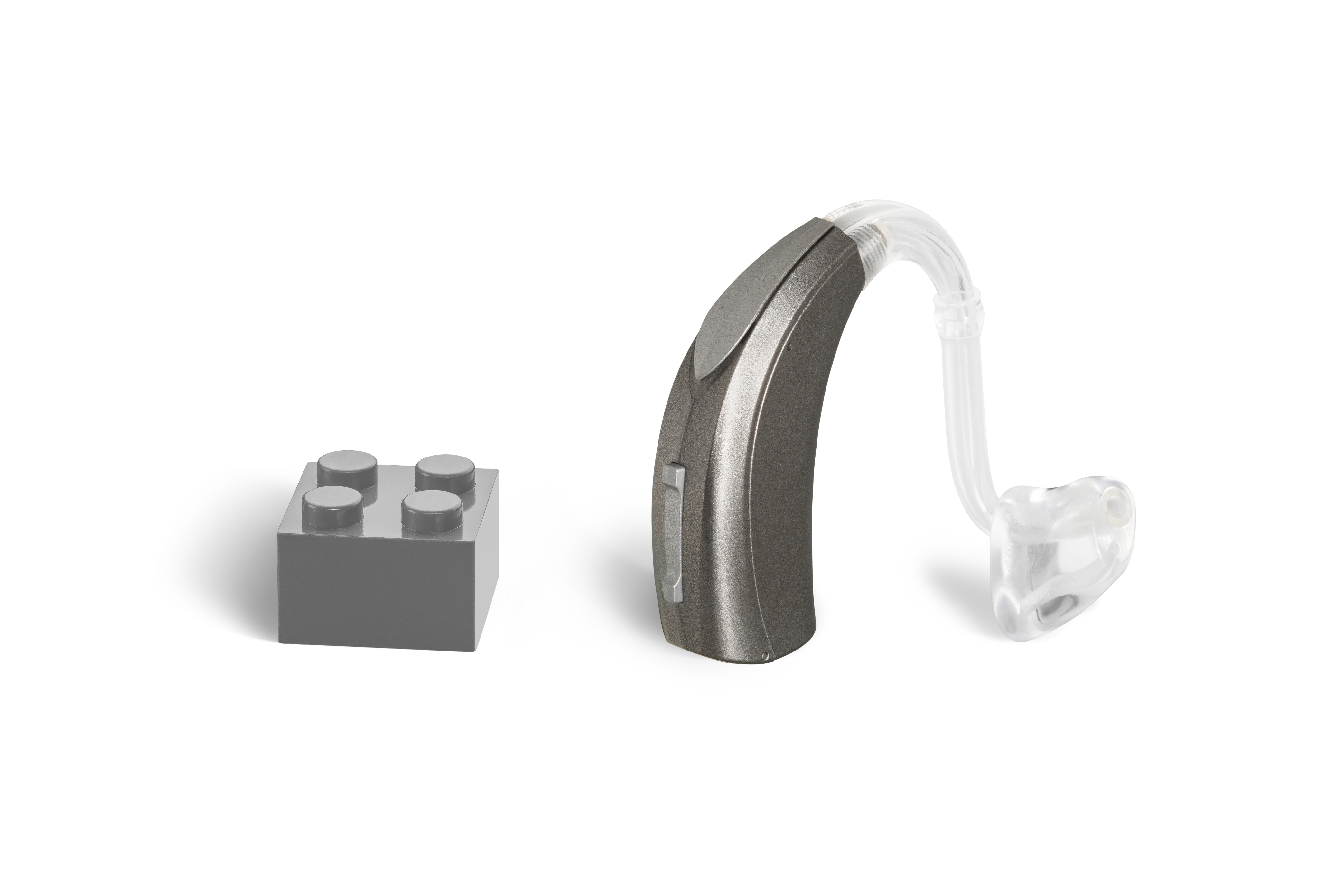 Das Hörgerät KINDvitalo 5120 als Bauform Power HdO mit Energieversorgung Batterie neben einem grauen Klemmbaustein stehend auf weißem Hintergrund.