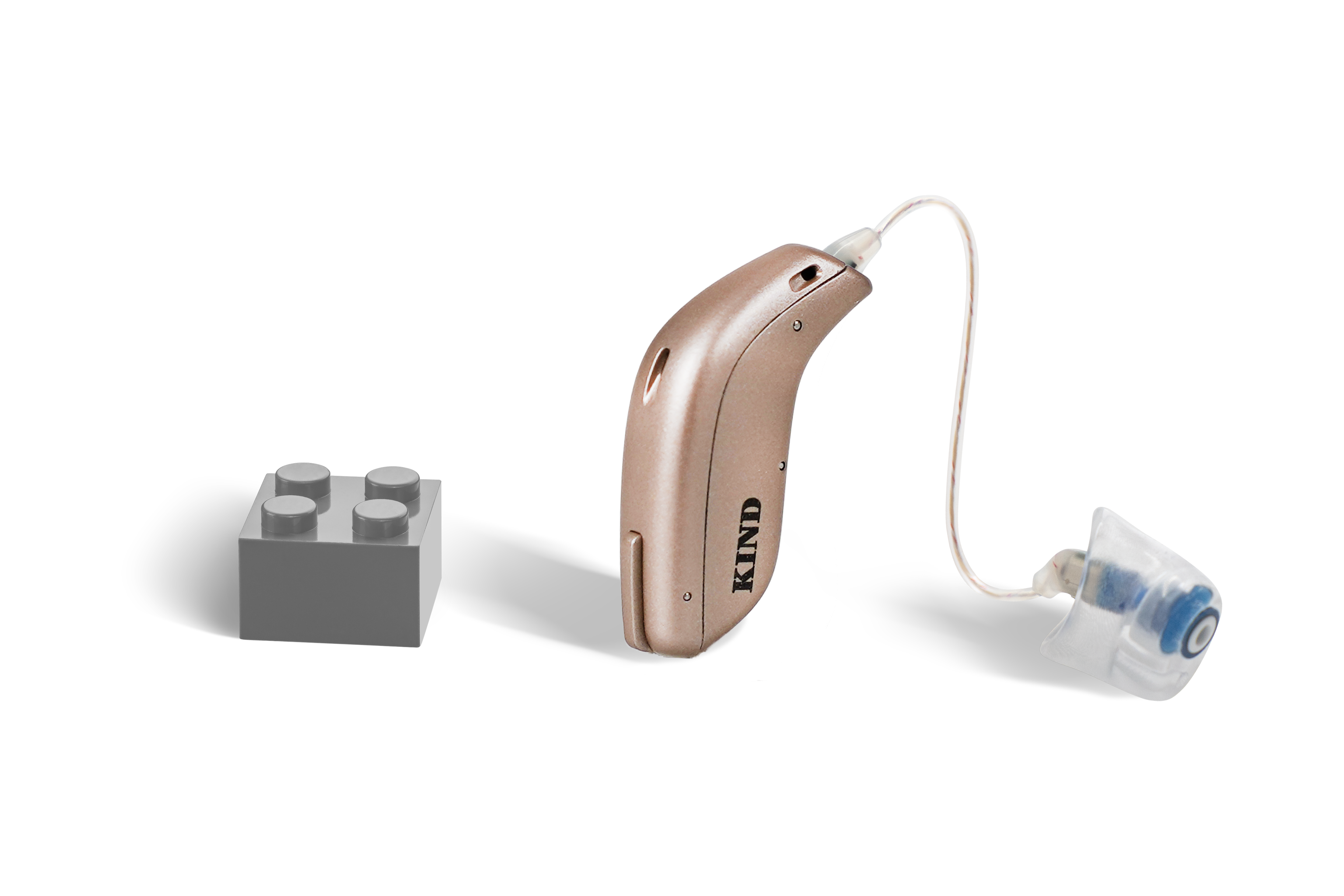 Das Hörgerät KINDduro 1400 als Bauform HdO mit externem Hörer mit Energieversorgung Batterie neben einem grauen Klemmbaustein stehend auf weißem Hintergrund.