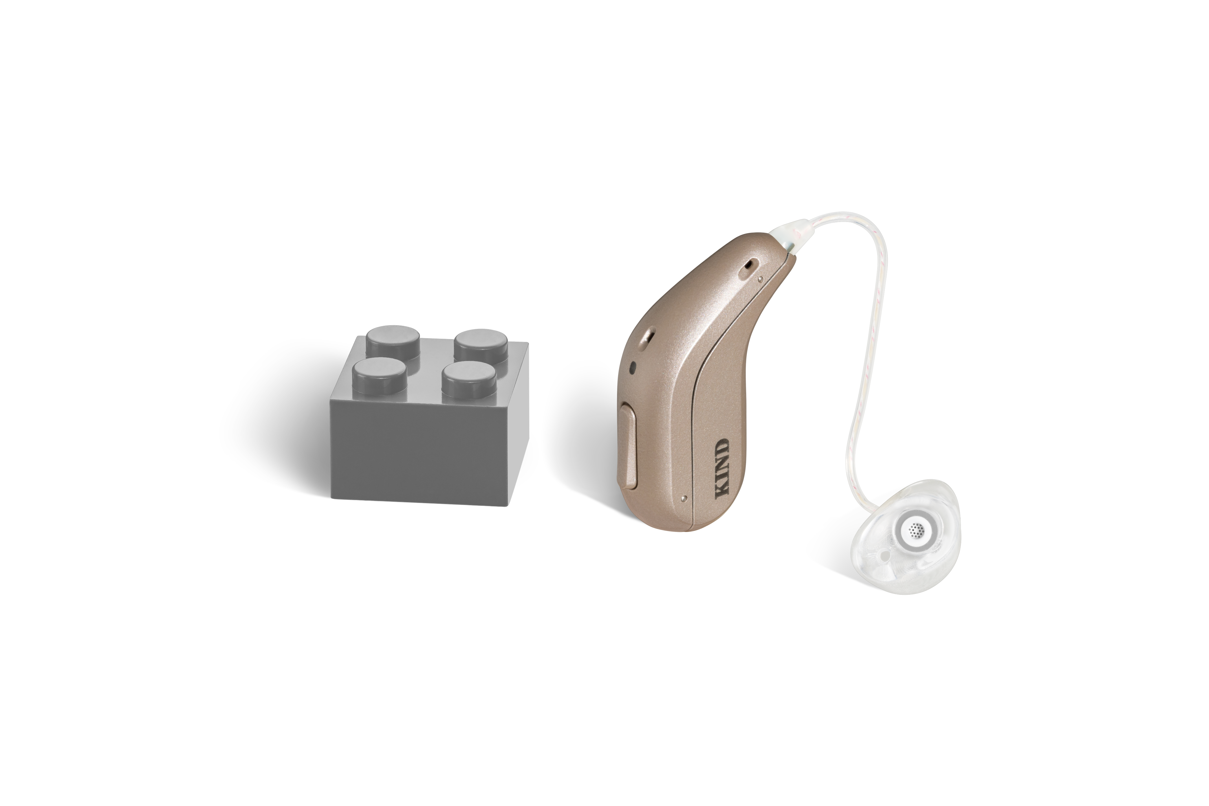 Das Hörgerät KINDsevan 5 miniRITE R als Bauform HdO mit externem Hörer mit Energieversorgung Akku neben einem grauen Klemmbaustein stehend auf weißem Hintergrund.