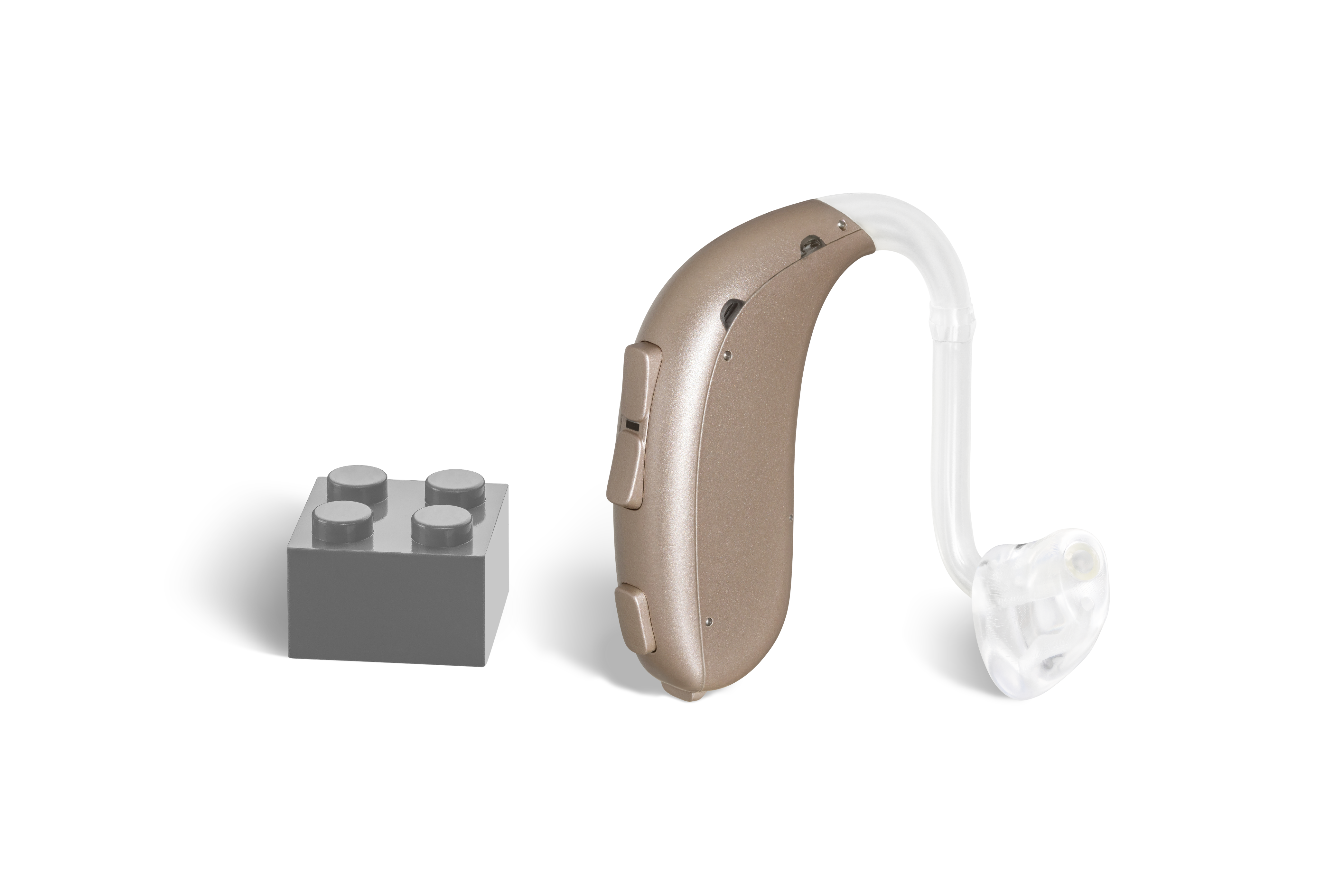 Das Hörgerät KINDsevan 4 miniRITE R als Bauform HdO mit externem Hörer mit Energieversorgung Akku neben einem grauen Klemmbaustein stehend auf weißem Hintergrund.