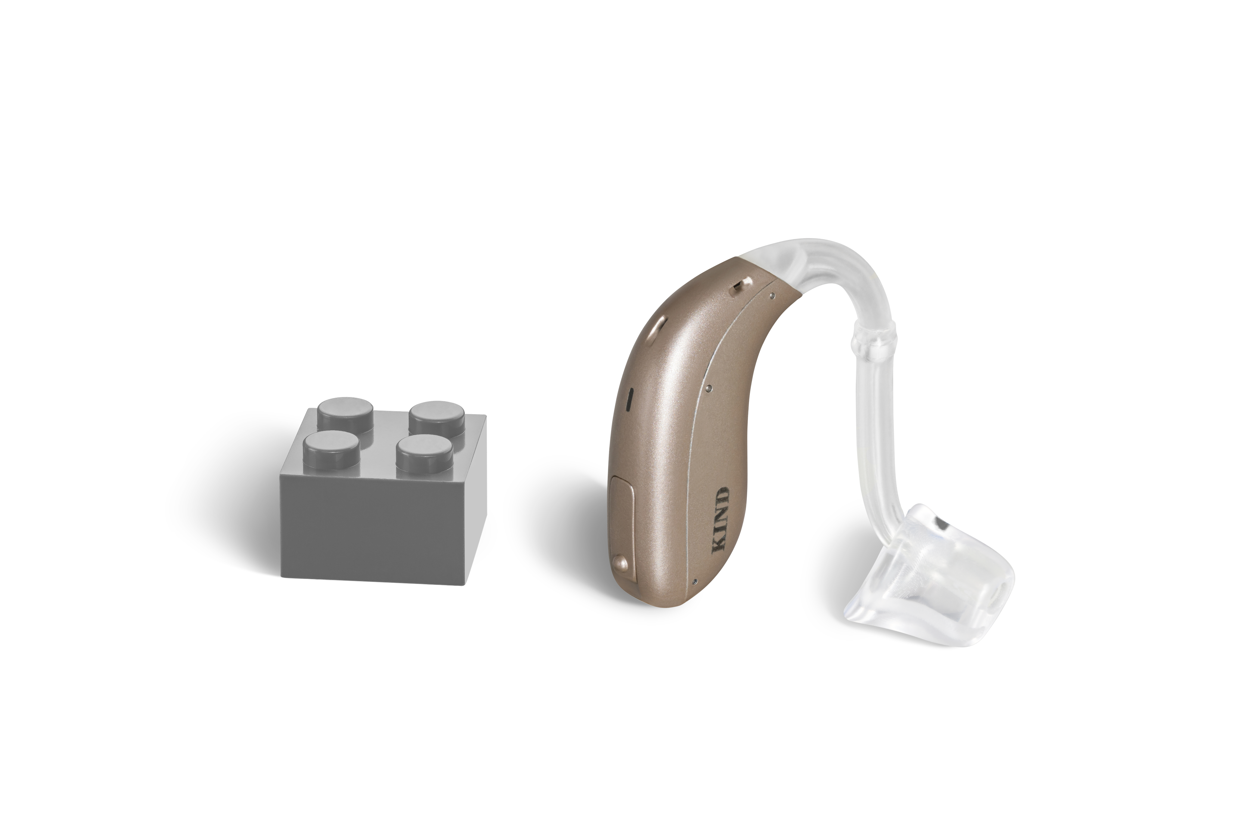 Das Hörgerät KINDsevan x 2 miniBTE C als Bauform Hinter dem Ohr mit Energieversorgung Batterie neben einem grauen Klemmbaustein stehend auf weißem Hintergrund.