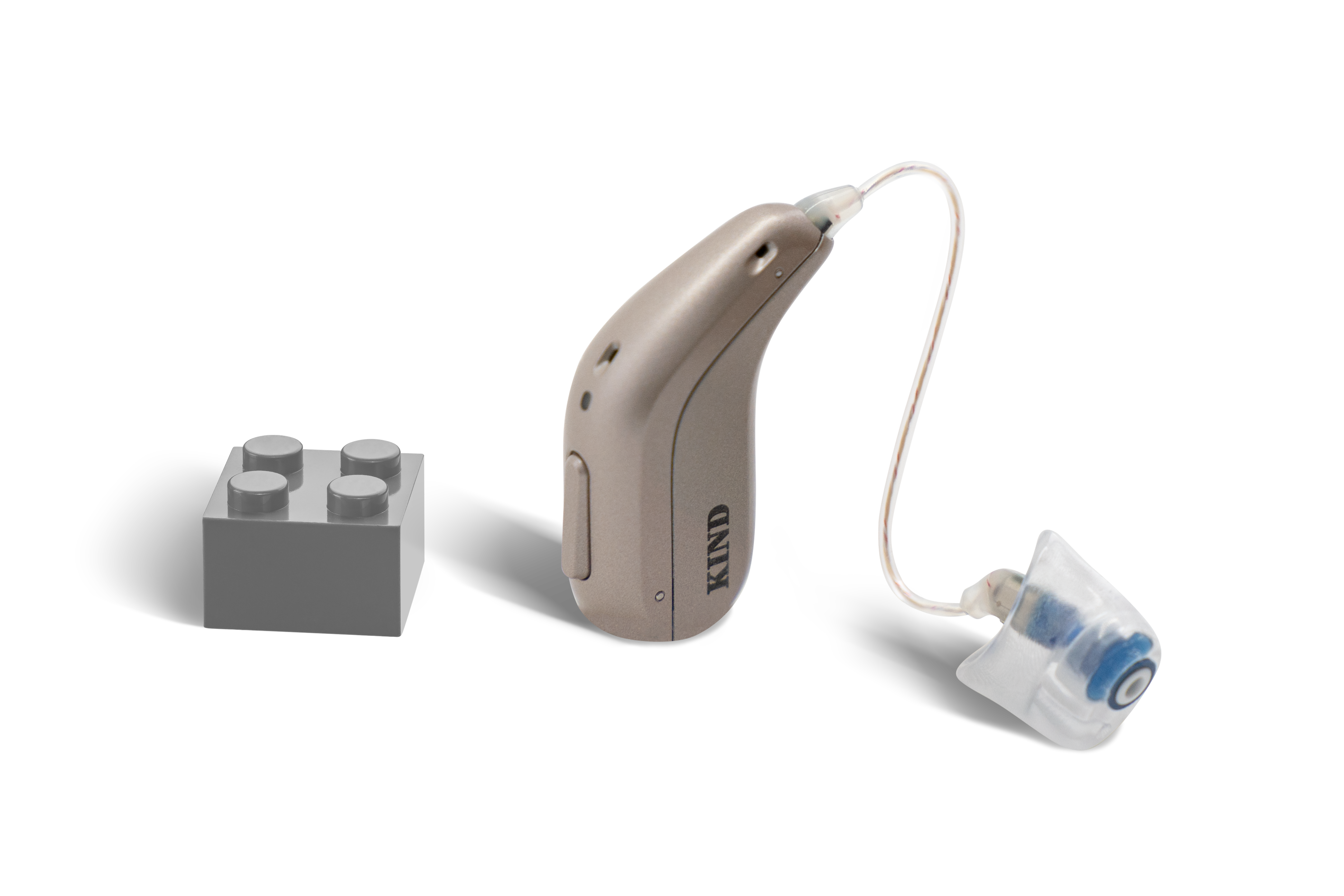 Das Hörgerät KINDsevan x 1 miniRITE R als Bauform HdO mit externem Hörer mit Energieversorgung Akku neben einem grauen Klemmbaustein stehend auf weißem Hintergrund.