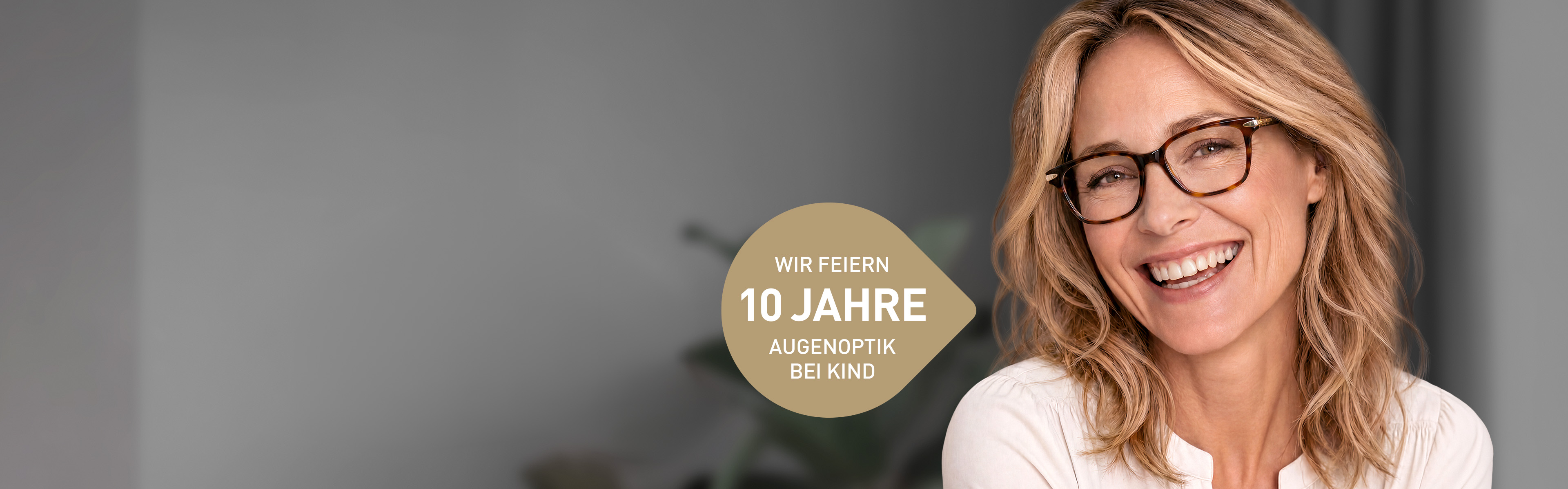 Frau mit Brille sitzt im Wohnzimmer und lächelt, dazu eine goldene Blase mit der Inschrift "Wir feiern 10 Jahre Augenoptik bei KIND"