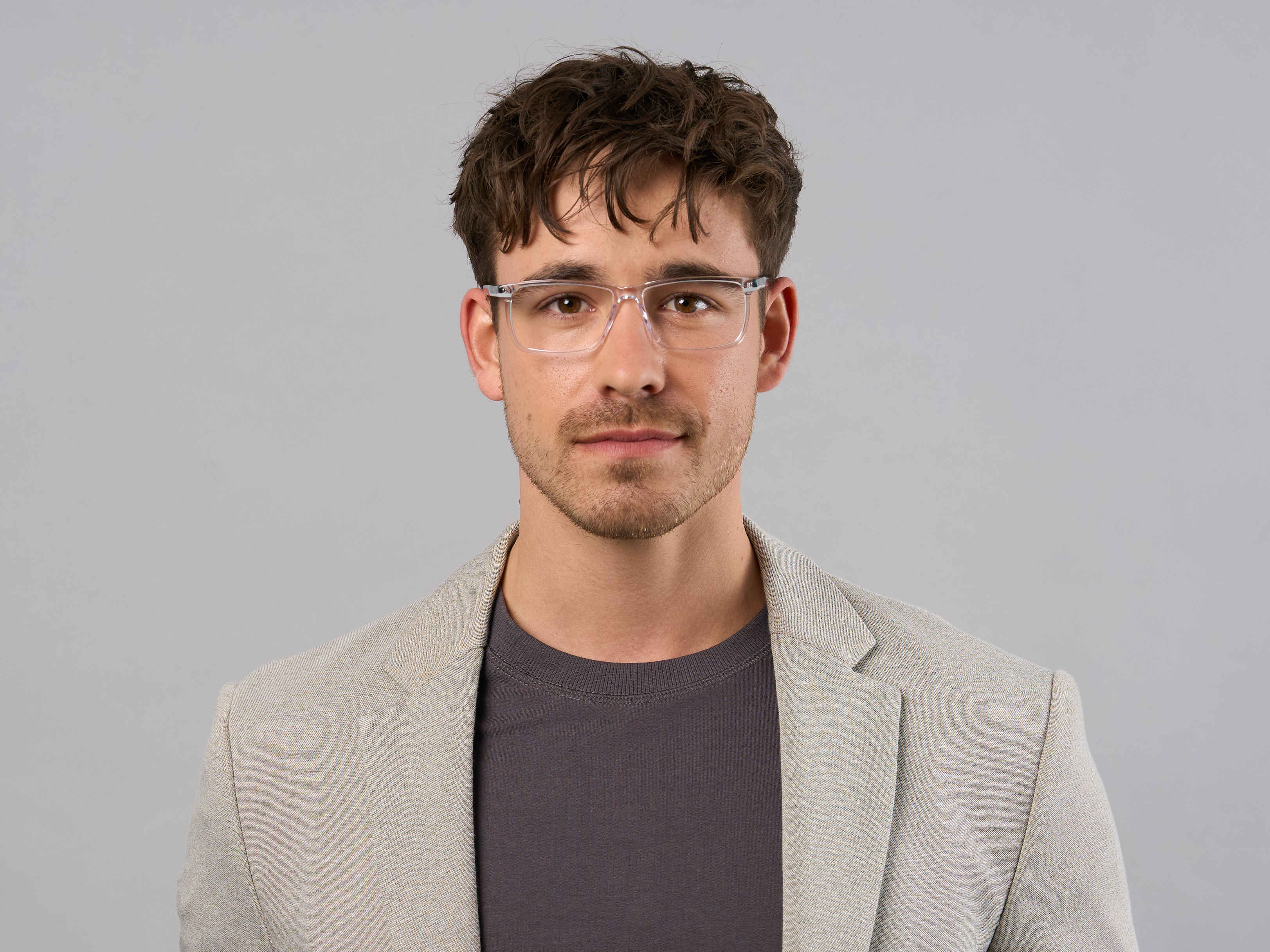 Herren-Model mit dunklem Shirt, hellem Sakko und einer transparenten, sportlichen Brille. 