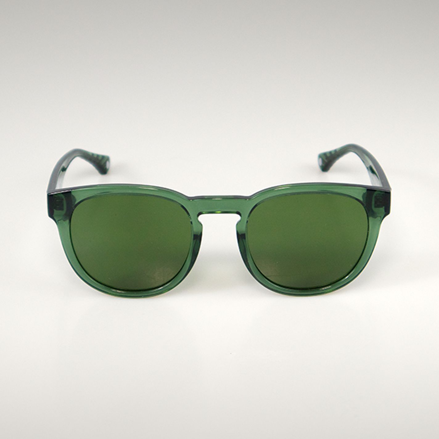 Eien grüne Sonnenbrille mit grünen Gläsern von vorne, darüber eine magentafarbene Blase mit dem Text "Gläser und Tönung inklusive".