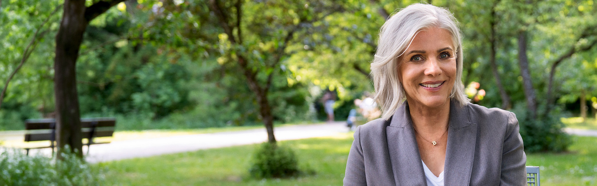 Birgit Schrowange sitzt im Park und lächelt den Betrachter an.