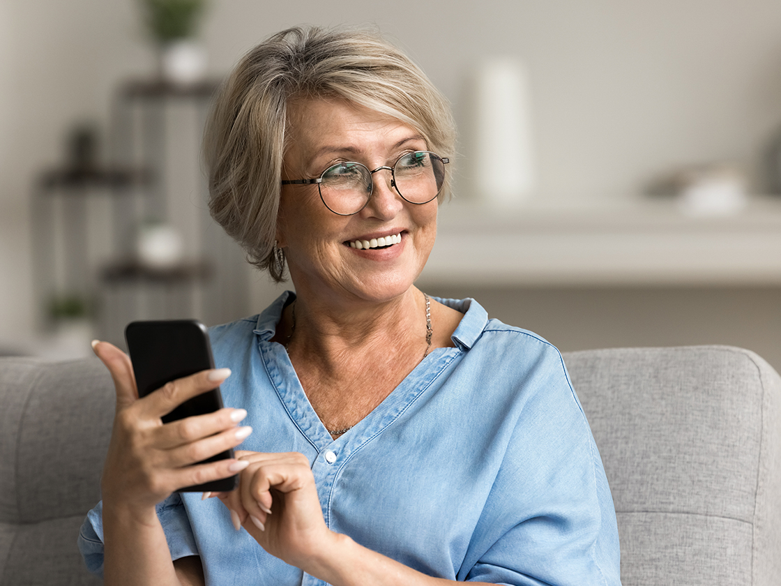 Frau im mittleren Alter sitzt mit Smartphone auf dem Sofa.