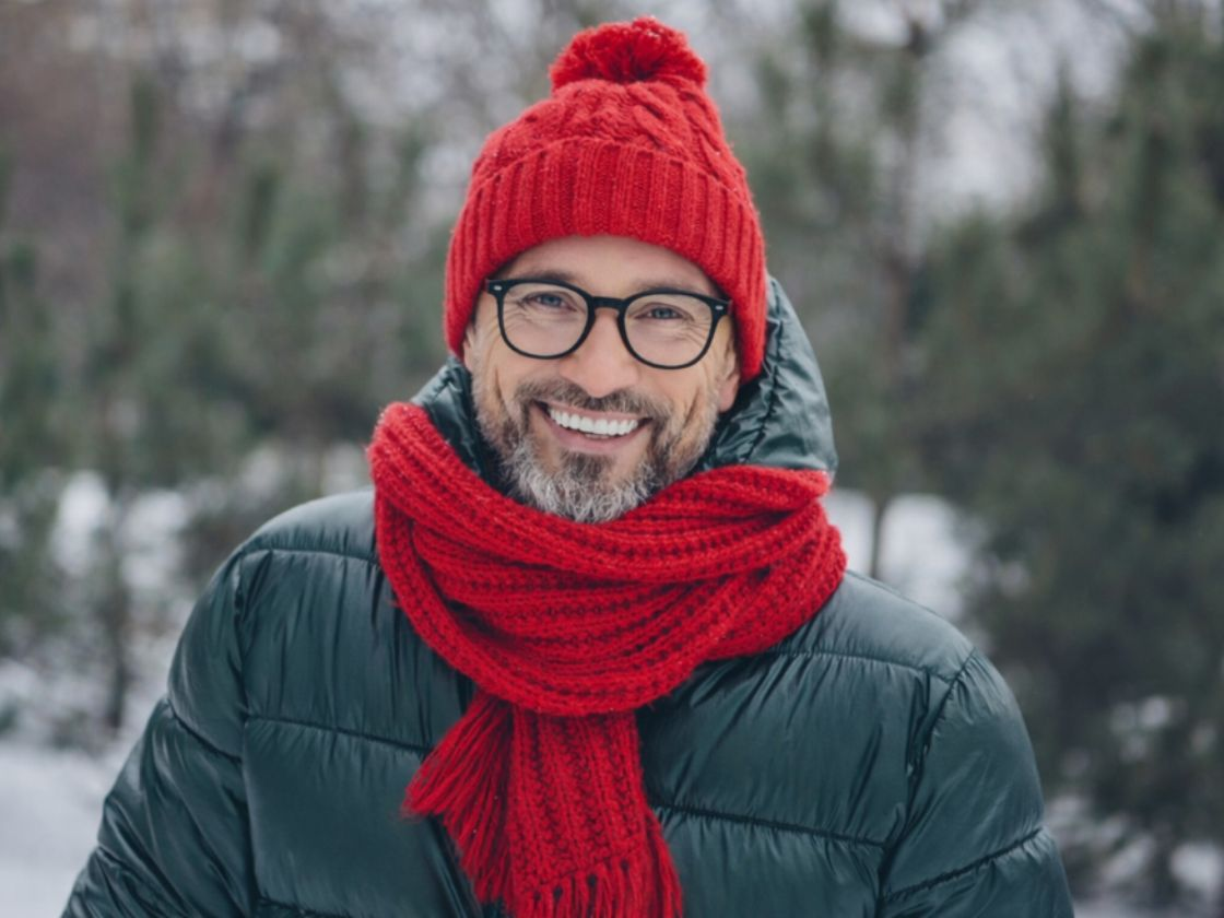 Mann im winterlichen Look mit winterlichem Hintergrund trägt eine schwarze Brille.