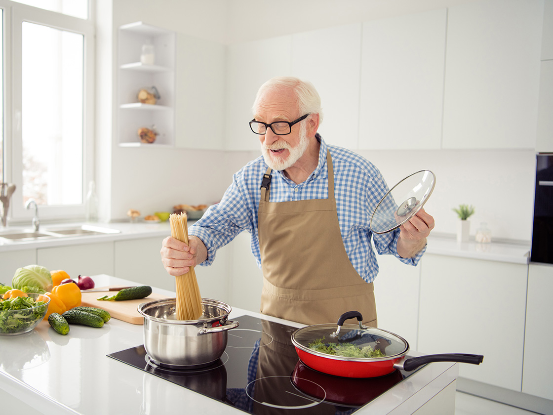 Ein älterer Mann steht in der Küche am Herd und kocht