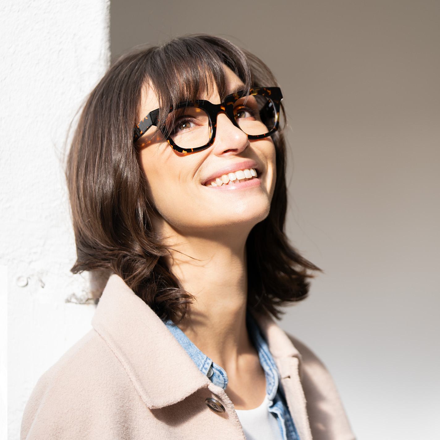 Weibliches Model trägt eine große schwarze Havanna-Brille, schaut nach oben und lächelt.