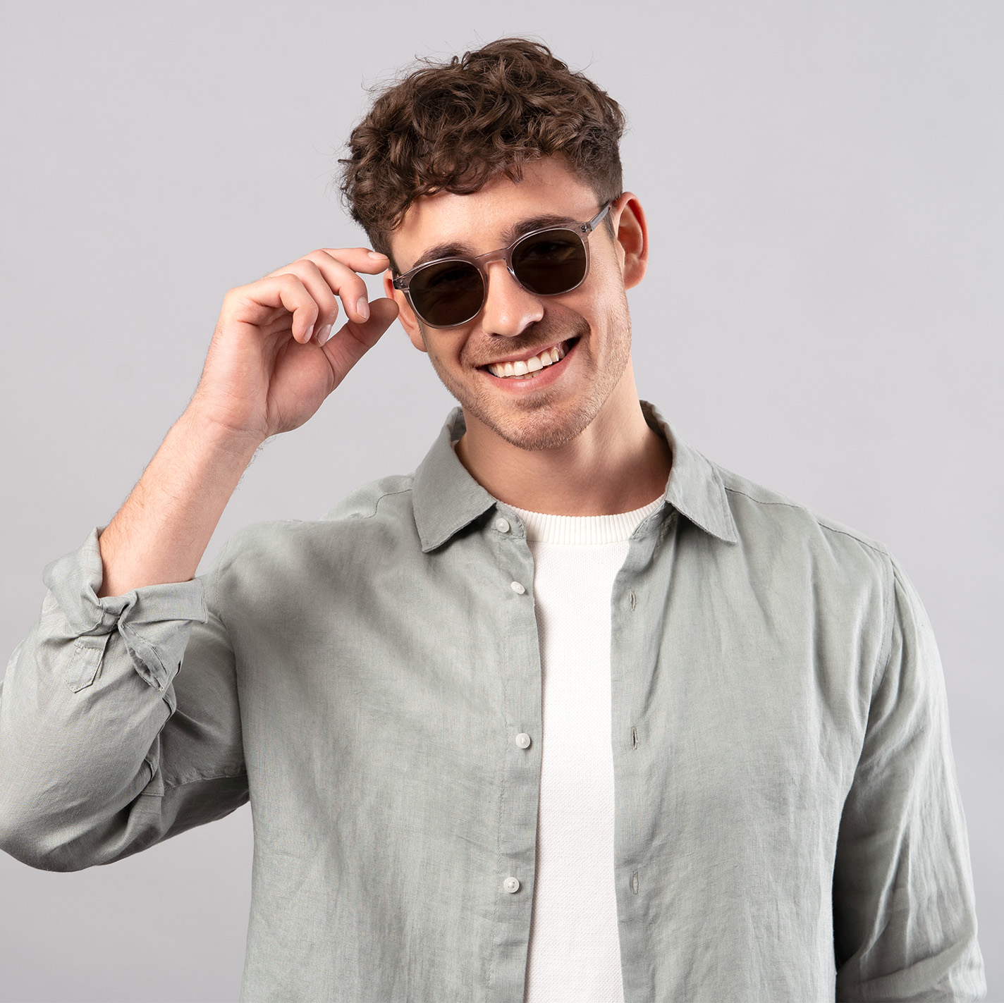 Männliches Model mit Sonnenbrille fasst sich an die Brille vor grauem Hintergrund