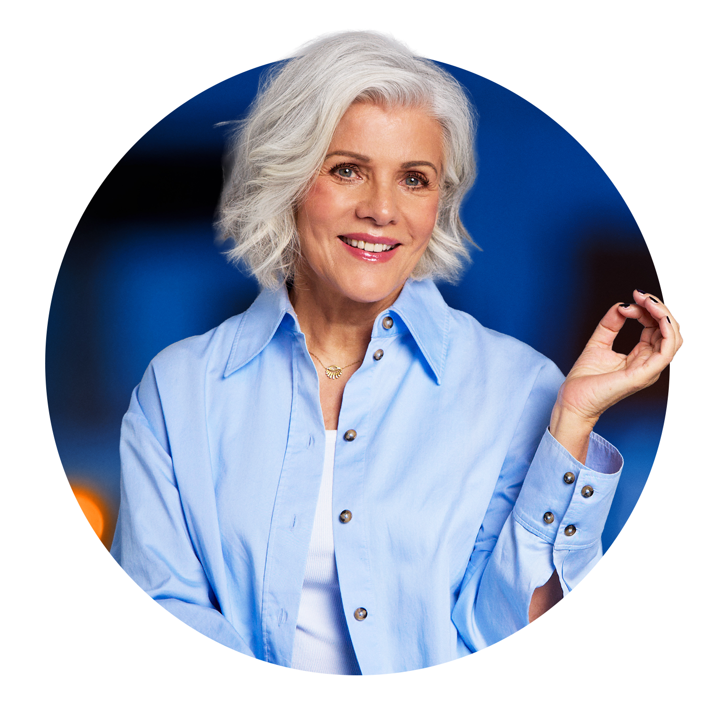 Birgit Schrowange vor blauem Hintergrund, lächelt und macht eine Handhaltung, bei der sich Daumen und Zeigefinger berühren.