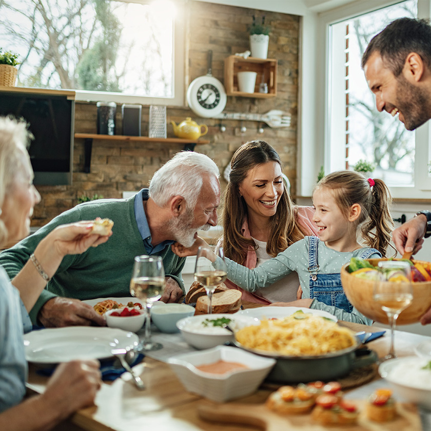 Familie mit Kindern, Eltern und Großeltern sitzen am Essenstisch und lachen zusammen. 